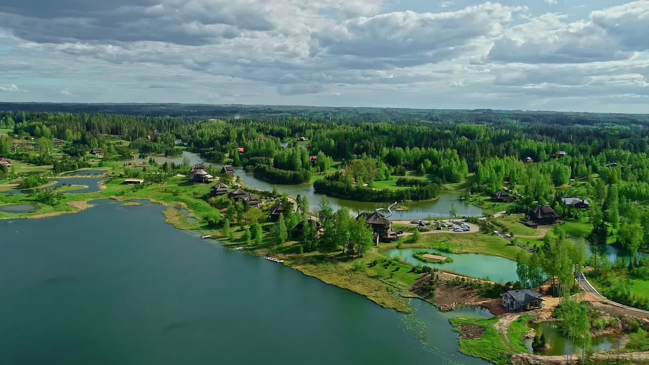 화창한 날 무성한 녹색 초목으로 둘러싸인 작은 연못과 호수 옆에 있는 아름다운 목조 오두막 위로 공중 드론이 촬영되었습니다.
