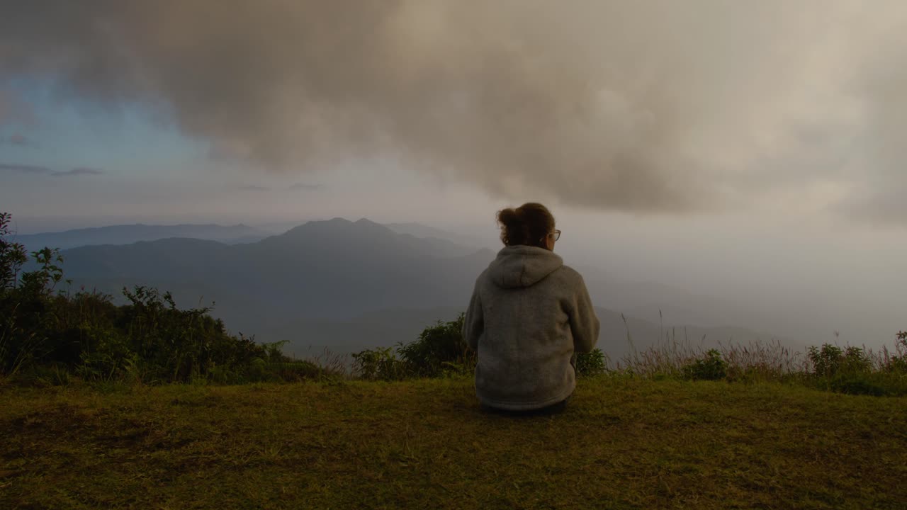 Person sitting on a hilltop overlooking misty mountains at dawn
