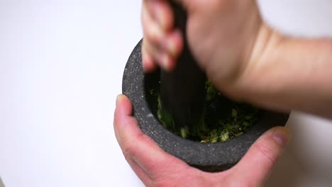 slow-motion of a mortar and pestle filled with fresh garlic, coriander, black peppercorns and salt to prepare a thai curry paste