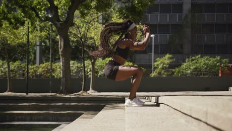 mujer afroamericana con auriculares inalámbricos haciendo ejercicio al aire libre saltando escaleras en la ciudad