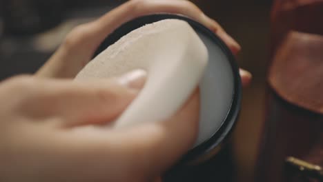 person rubbing a white sponge unto wax to polish a leather bag