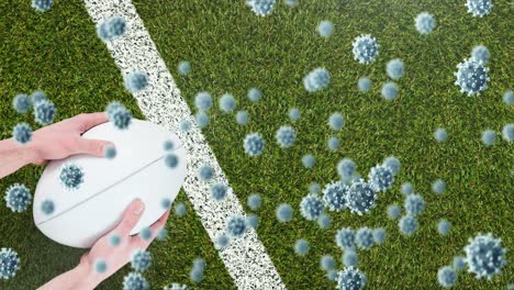 animation of virus cells over hands of caucasian player holding rugby ball on stadium