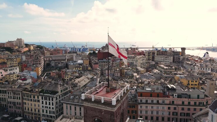 Veduta aerea della storica città di Genova con la sua bandiera iconica e il porto in una giornata parzialmente nuvolosa.