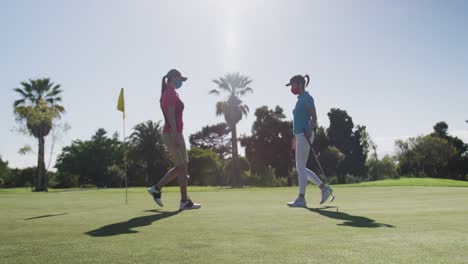 Two-caucasian-women-playing-golf-wearing-face-masks-greeting-each-other-with-feet