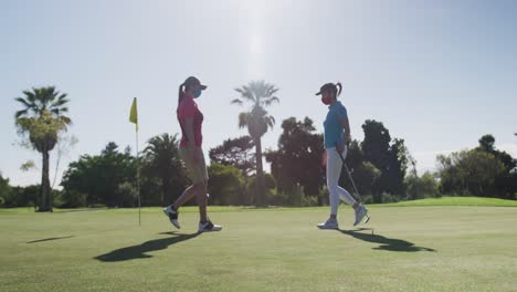 two caucasian women playing golf wearing face masks greeting each other with feet