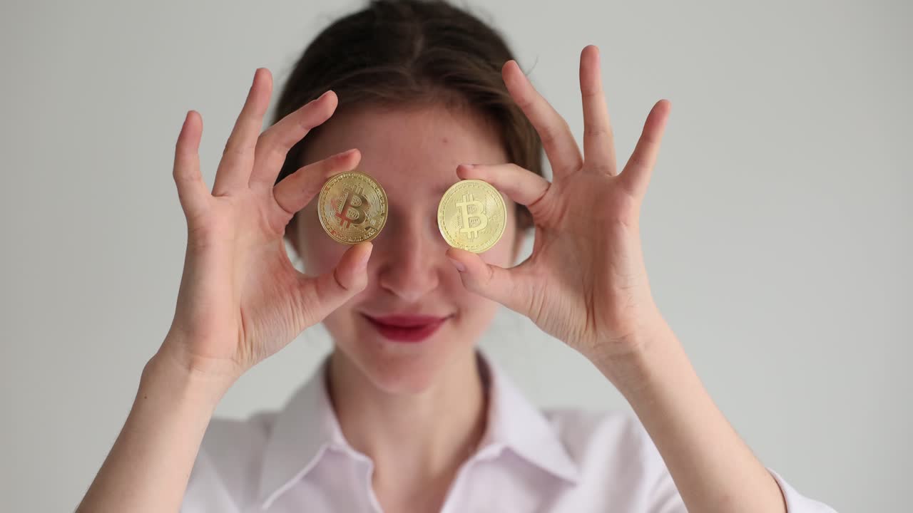 Mulher satisfeita coloca moedas com símbolos de Bitcoin sobre os olhos.