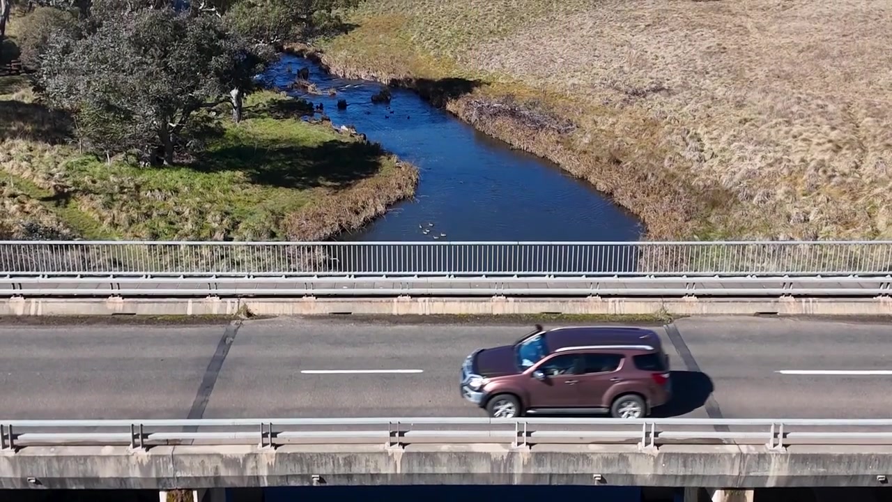 Imágenes de dron capturan un SUV oscuro cruzando un puente rural sobre un arroyo azul