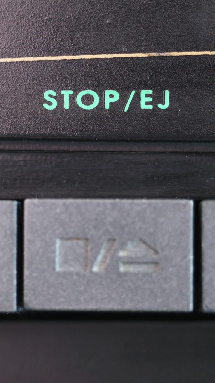 Primo piano verticale di un pulsante grigio di stop/espulsione che viene premuto sotto la scritta turchese STOP EJ.