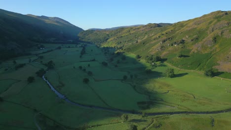 shadowed valley with patchwork fields and winding stream on sunny summer morning in the english lake district, cumbria, uk