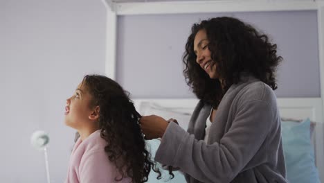 Happy-mixed-race-mother-and-daughter-brushing-hair-in-bedroom