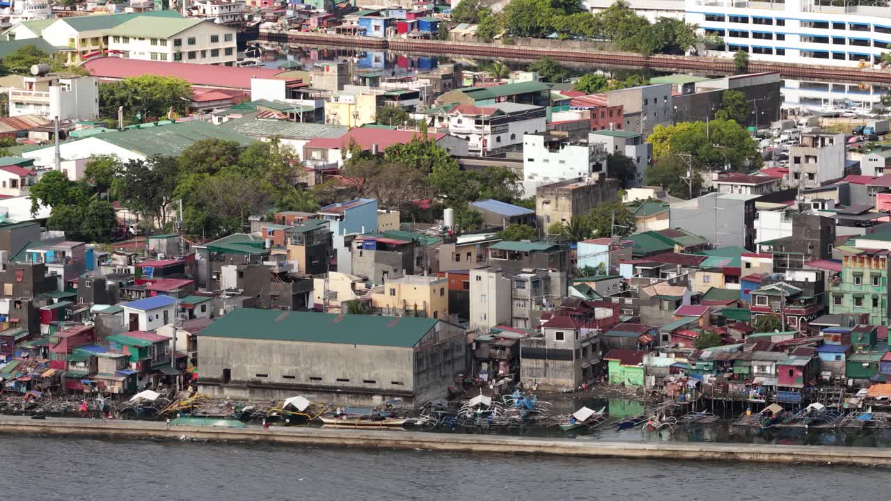 Manila, Filipinler'de bir nehir boyunca yer alan, yayılmış, fakir bir gecekondu mahallesi bölgesinden geçen bir banliyö treninin hava görüntüsü, kentsel yoğunluğu ve yoksulluğu vurguluyor