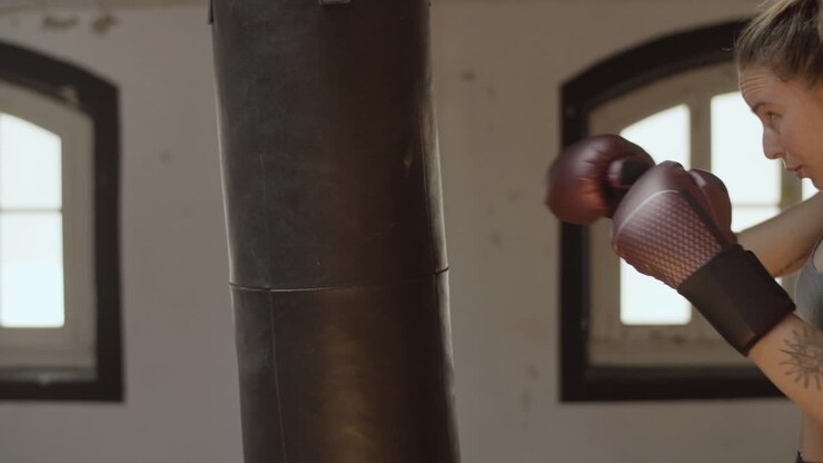 Vista laterale di una donna seria che colpisce un sacco da boxe in una sala di allenamento