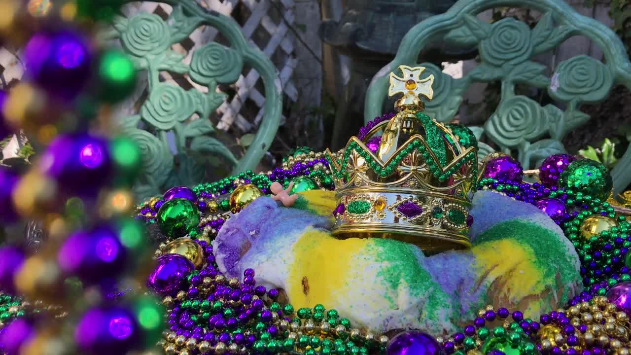 hilos de cuentas que enmarcan el pastel de mardi gras king con corona y un pequeño bebé rodeado de coloridas cuentas y luz solar moteada