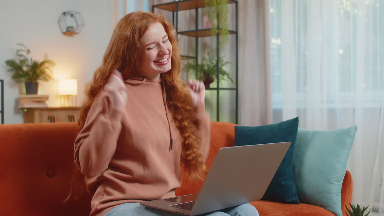 mujer emocionada sentada en el sofá usando una computadora portátil recibe buenas noticias victoria celebrar la victoria de la lotería en casa