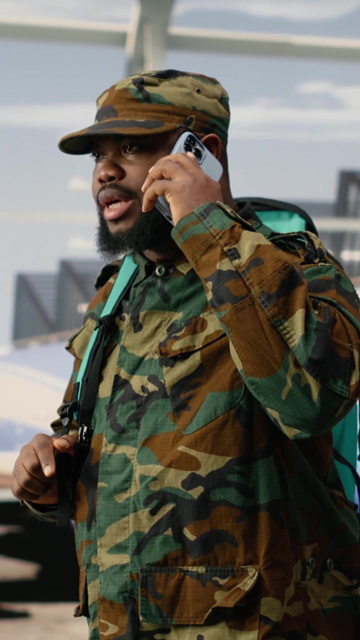 Video verticale. Soldato dell'esercito che telefona con il cellulare in aeroporto, preparandosi per il ritorno a casa.