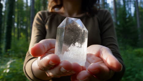 person holding a clear crystal in a forest