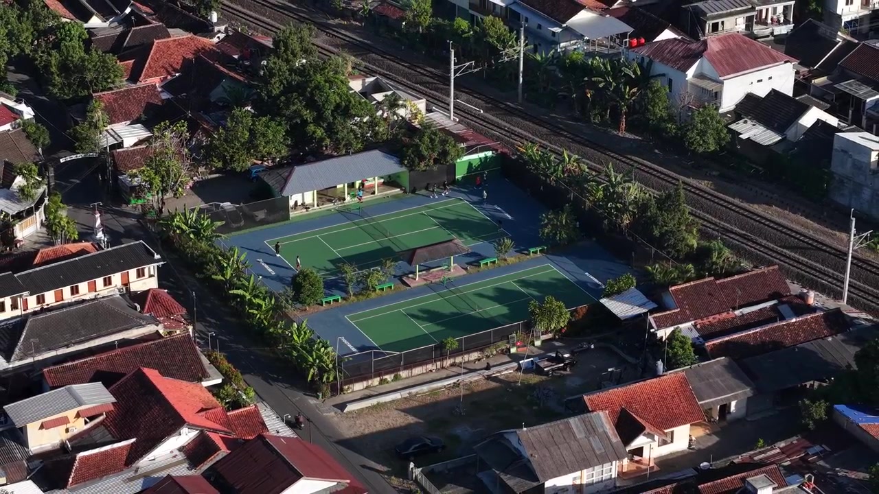 Morgenluftfoto af en tennisbane mellem et byområde og kanten af en jernbanelinje i Yogyakarta, Indonesien.