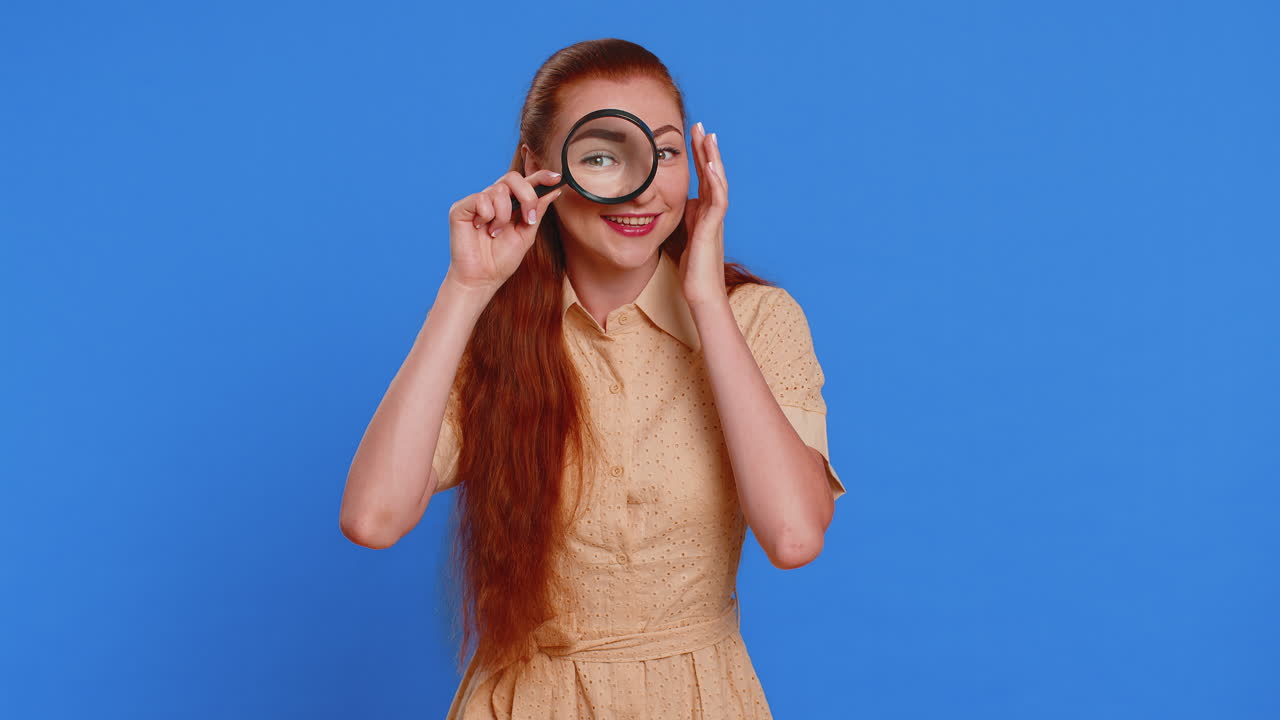 Investigator woman holding magnifying glass near face looking into camera with big zoomed funny eye