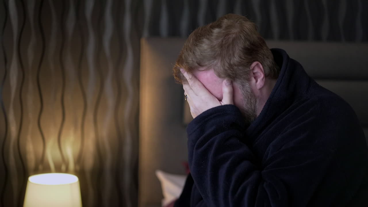 Depressed man sitting on edge of bed with head in hands
