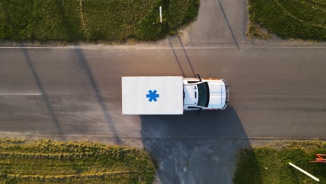 aerial top-down shot of ambulance driving across screen slowly on road with emergency lights on