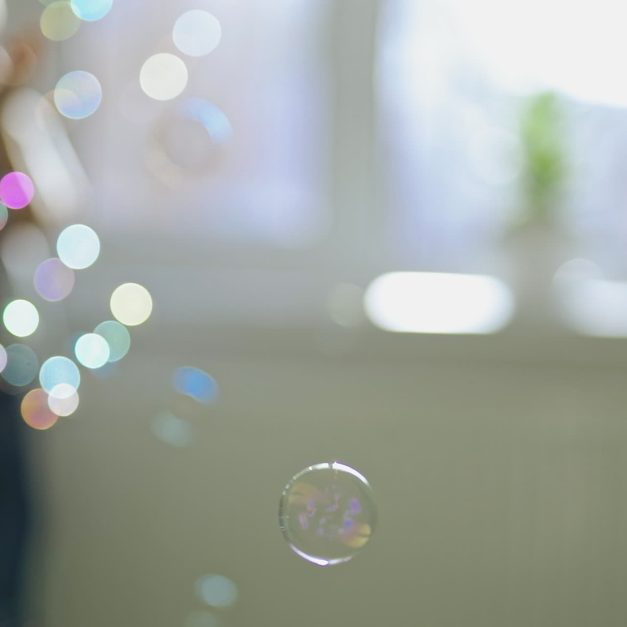 Round colorful bubbles flying in the room on the blurred background with a boy. Beautiful soap bubbles and a silhouette of a boy playing with them indoors.