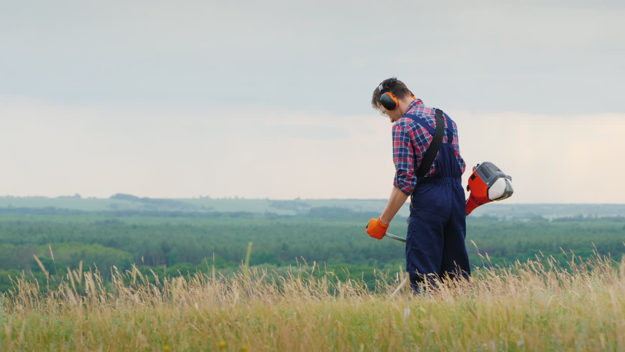 한 남자가 그림 같은 곳에서 트리머로 두꺼운 풀을 깎고 있다