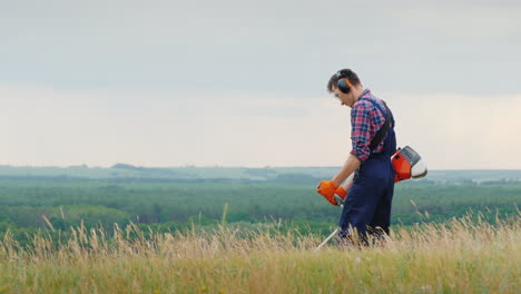 a man mows thick grass with a trimmer in a picturesque place