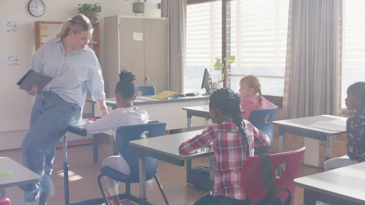 In school, female teacher interacting with students in classroom, holding tablet