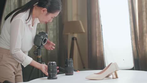 asian female photographer changing camera's lens while taking photos of women's shoes in home studio