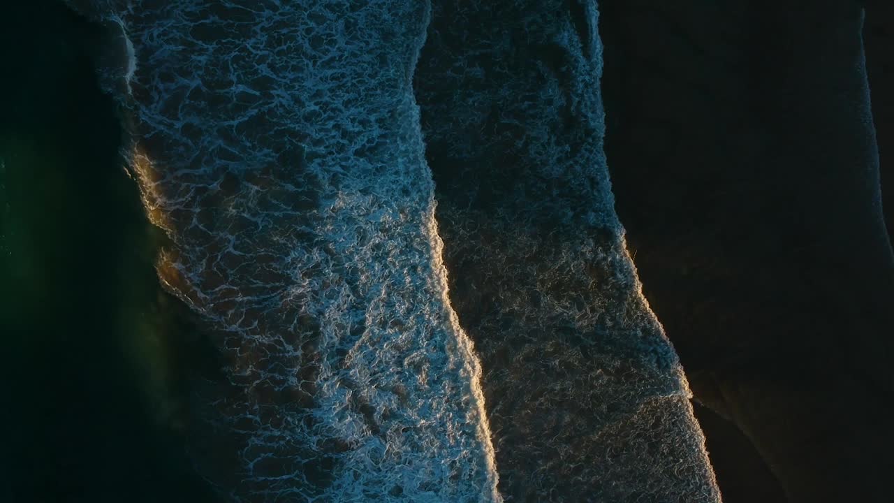 Waves breaking on a dark beach with the sunlight breaking through