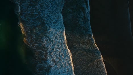 Waves-breaking-on-a-dark-beach-with-the-sunlight-breaking-through