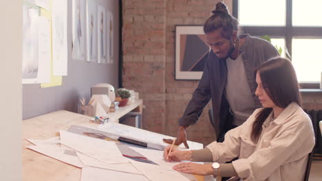 female graphic designer sitting at drawing desk and discussing new project with her colleague in an animation studio 1