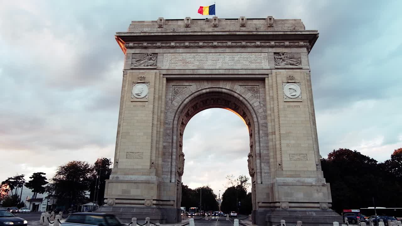 Bucharest, Romania - April 24, 2021: Cars moving near The Triumphal Arch at sunset