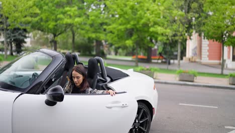 mujer conduciendo un coche descapotable blanco en la ciudad