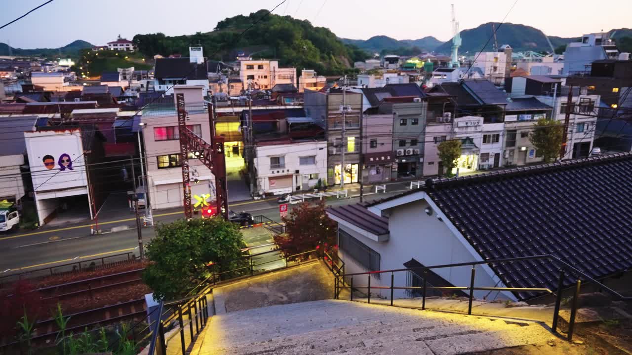 Sunset over small port town in Japan's inland sea, JR Train passes road and homes in the evening