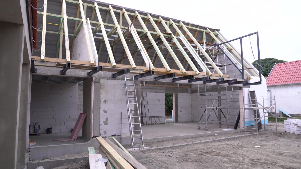 House structure with exposed roof trusses, concrete block walls, and scaffolding on a construction site