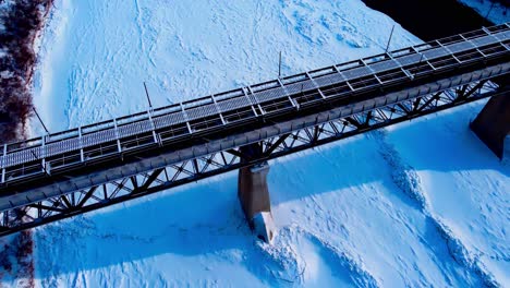 winter afternoon aerial flyover drop dolly roll birds eye view over high level bridge as person walks on pedestrian designated path overlooking the snow covered northh saskatchewan river blu4-4