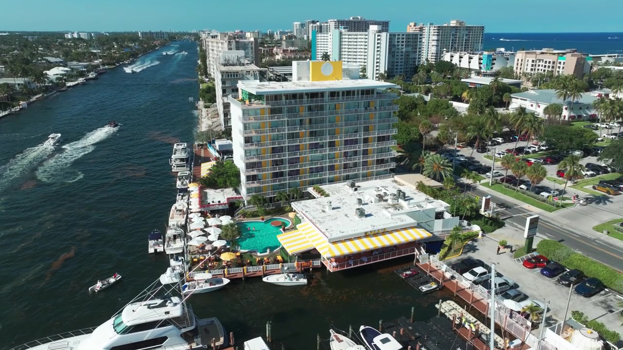 Riprese aeree con drone del vivace Lola's on the Water a Pompano Beach, che mostrano la ristorazione sul molo, barche di lusso, una terrazza piscina tropicale e il trafficato Intracoastal Waterway.