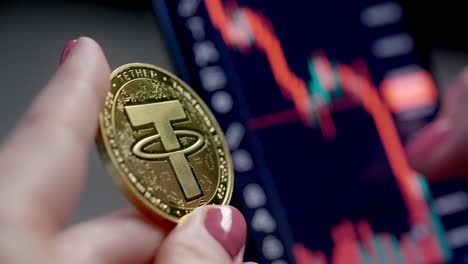 dedo femenino sujetando la moneda de criptomoneda dorada contra el gráfico de precios de las acciones financieras en la pantalla