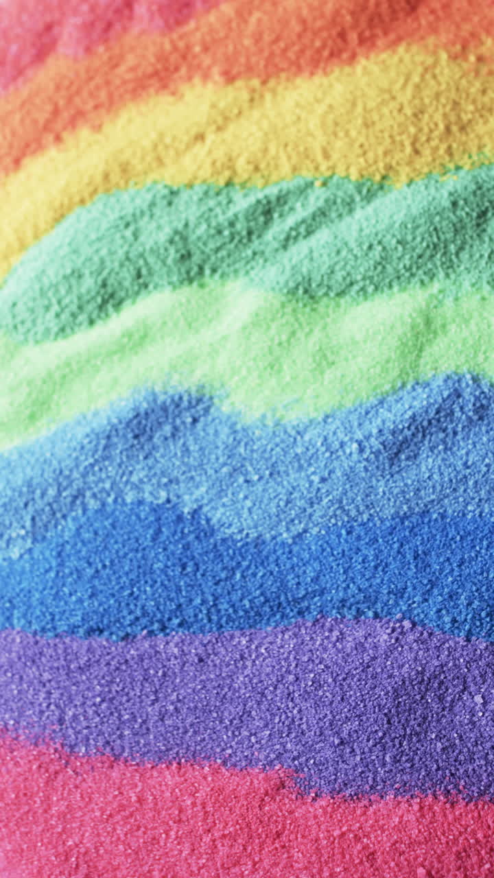 Vertical video of close up of rainbow coloured sand grains and copy space background