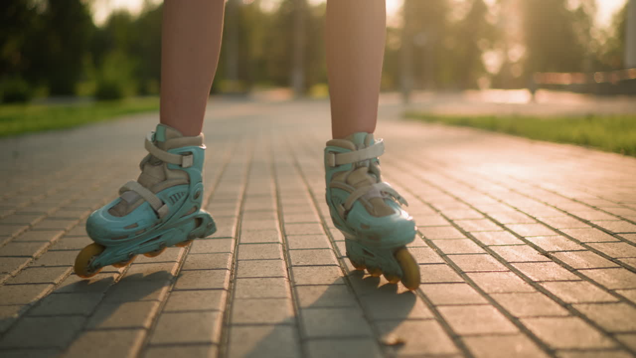 Leg view of person roller skating on interlocked path, wearing teal rollerblades, with shadow cast on ground by warm sunlight, blurred background with lush greenery and trees