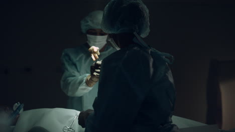 nurse handling sterile instruments dark room closeup. medical team cooperation