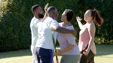 celebrating victory, diverse friends giving high fives on tennis court holding rackets