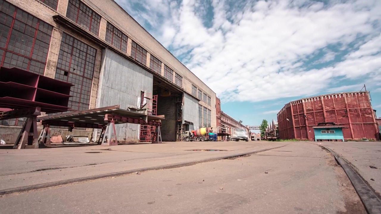 Timelapse hyperlapse del antiguo edificio del almacén de la fábrica con puertas. Vista del edificio en la zona industrial de una gran planta con raíles en el asfalto.
