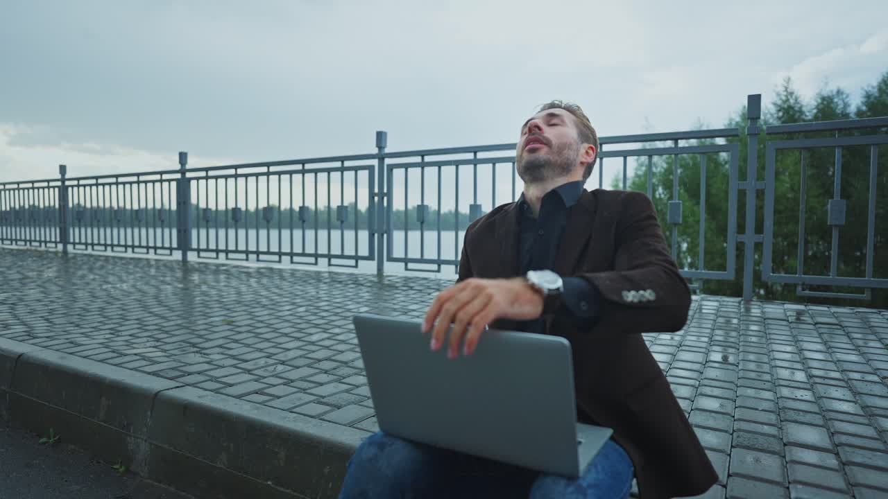 Uomo che lavora al portatile all'aperto sotto la pioggia