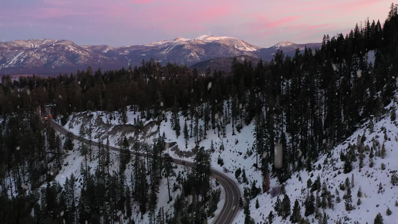 carretera montañosa rodeada de densos bosques durante las nevadas en invierno, vista aérea ascendente