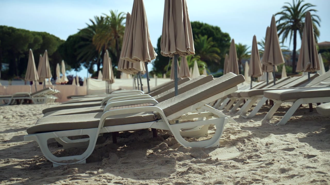 Rows of sun loungers and folded umbrellas await guests on a sandy beach, ready for vacation relaxation