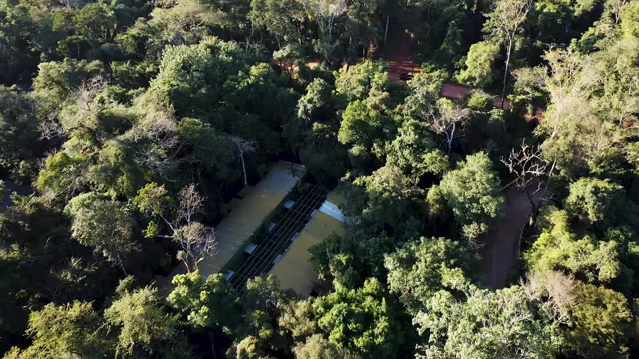 Downward daisy cutter drone view portraying hotel in the middle of the jungle, with beautiful green trees and reddish dirt road on back. Shot on 4K at 60fps.