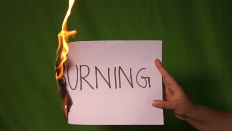 a hand holds the burning paper with burning text in single lines word on it