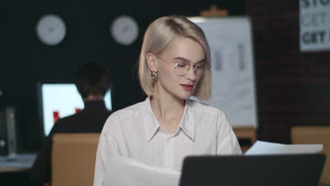 Thoughtful-business-woman-reading-document-on-laptop-in-dark-office.